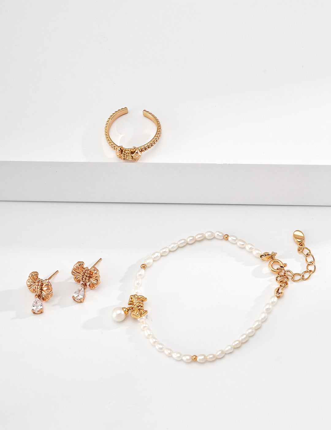 Gilded bow ring. Its crinkled texture brings an innate vintage charm, accented with dangling teardrop zircon stones that embody sophisticated grace.
