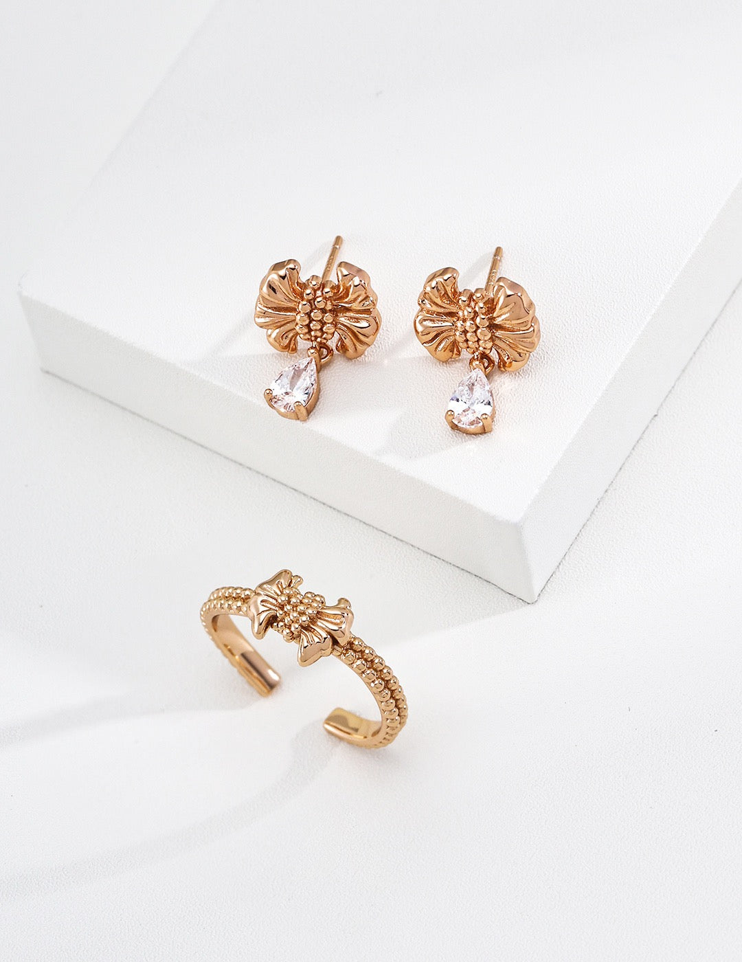 Gilded bow ring. Its crinkled texture brings an innate vintage charm, accented with dangling teardrop zircon stones that embody sophisticated grace.