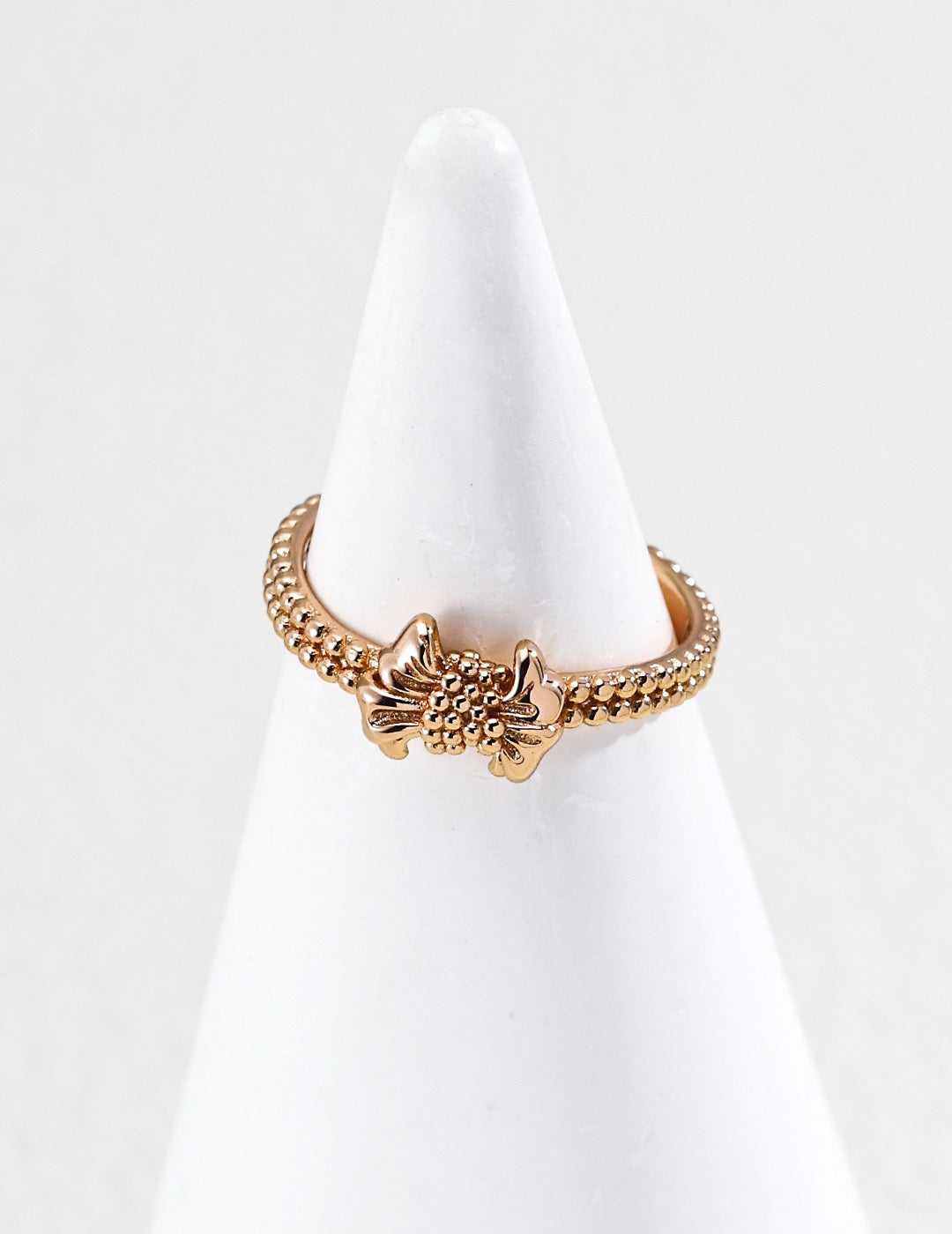Gilded bow ring. Its crinkled texture brings an innate vintage charm, accented with dangling teardrop zircon stones that embody sophisticated grace.